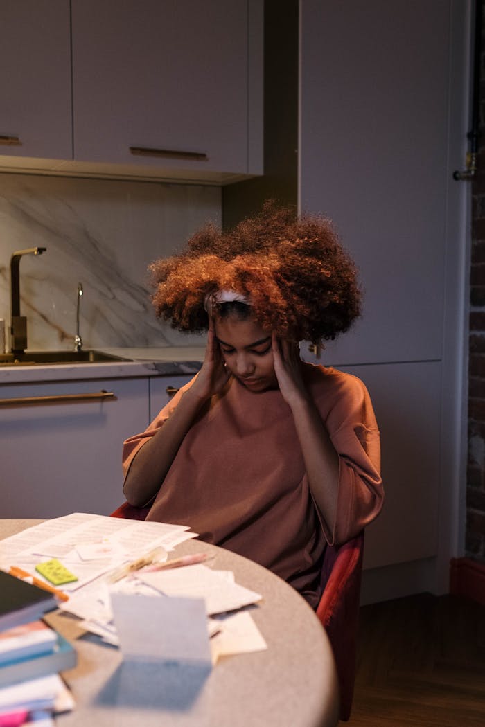A young woman with afro hair looks exhausted while studying at her kitchen table.