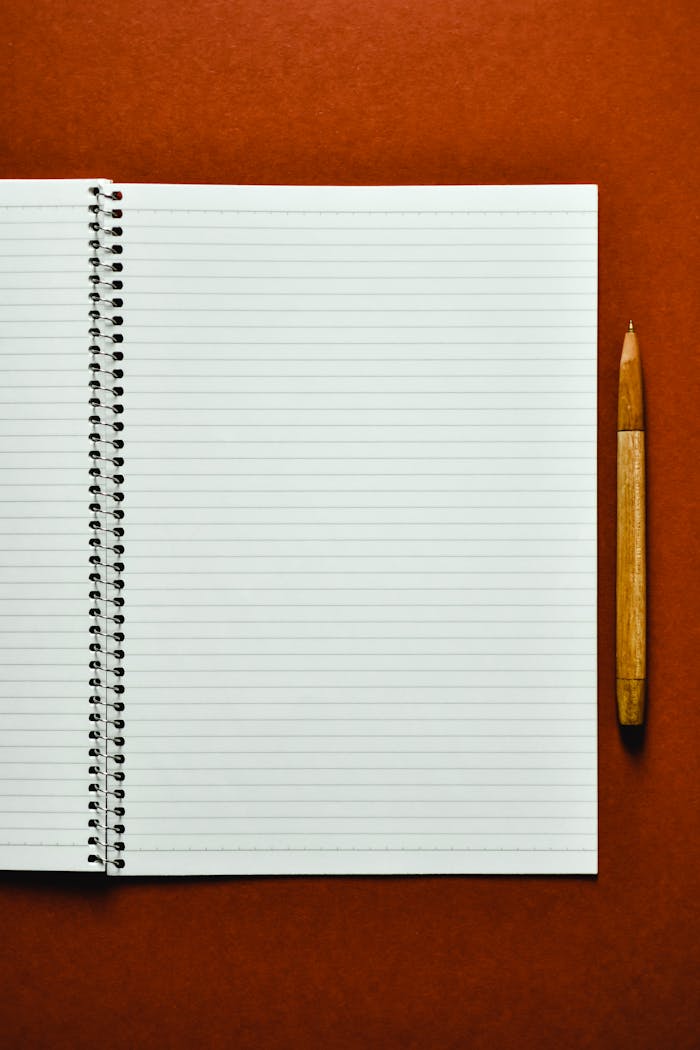 Open spiral notebook and wooden pen on orange surface, ideal for artistic presentations or school-related content.